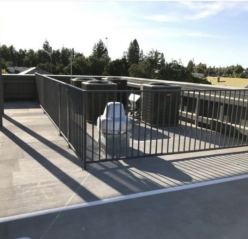 Rooftop with HVAC units behind a black metal fence. Blue sky and trees in the background.