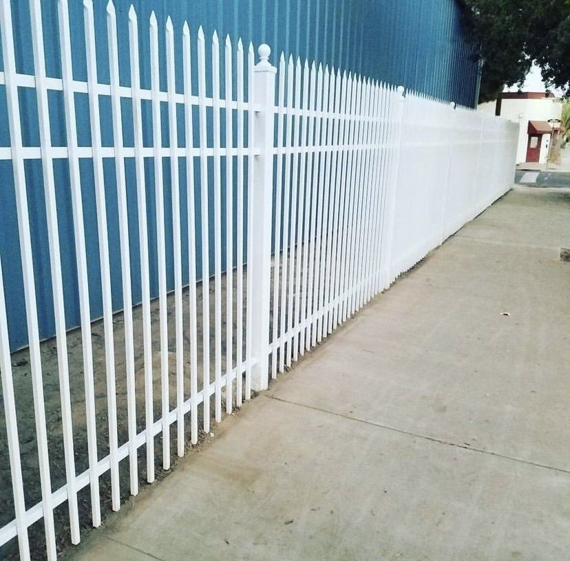 White metal picket fence along a sidewalk next to a building with a blue exterior.