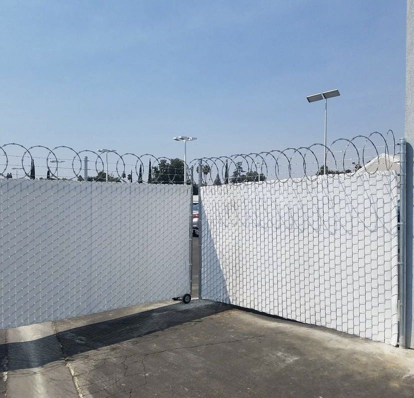 White security gate with razor wire on top, under a blue sky.