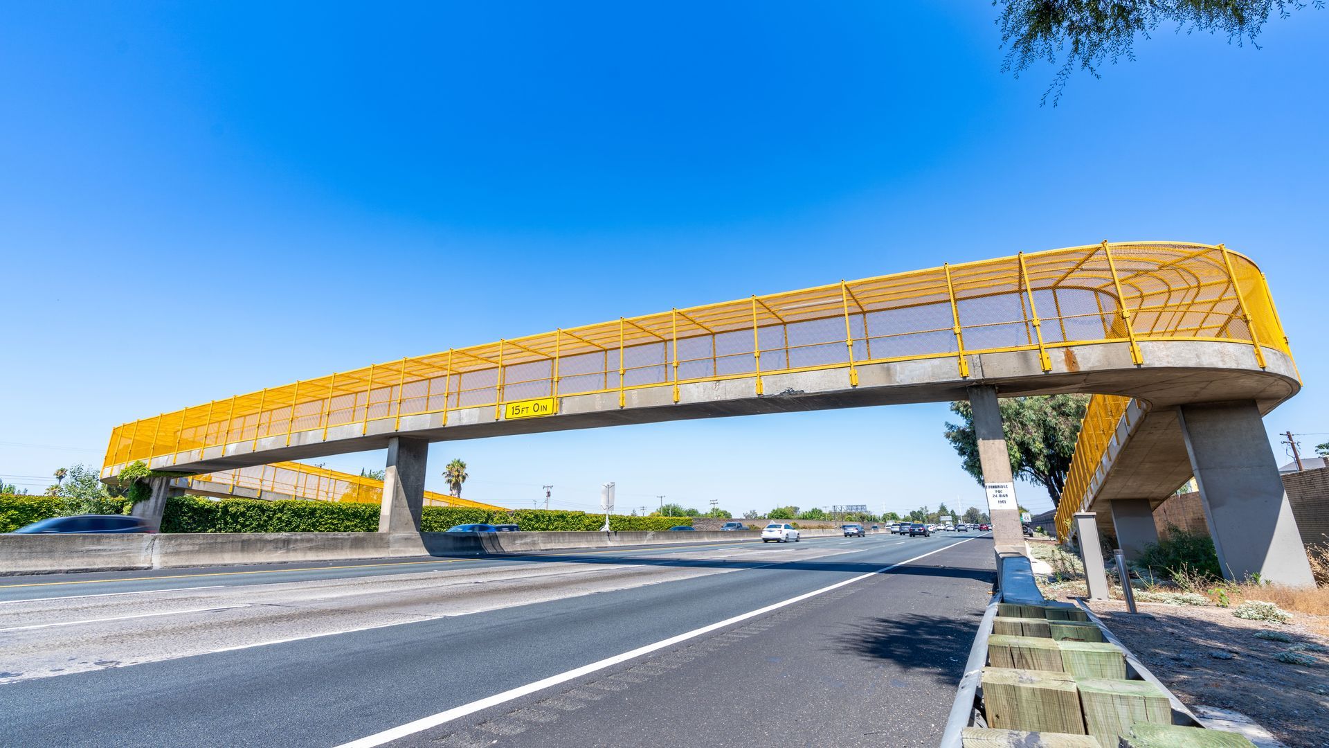 Yellow pedestrian bridge over a highway on a sunny day.