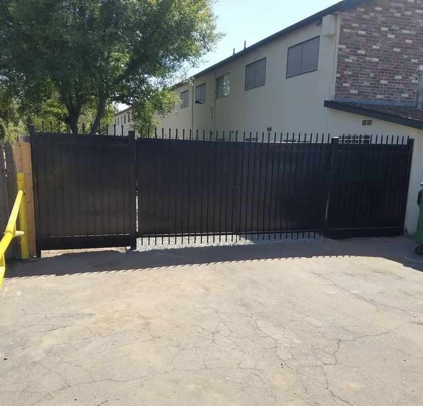 Black metal gate in front of a building, the gate is closed with vertical bars and a spiked top.