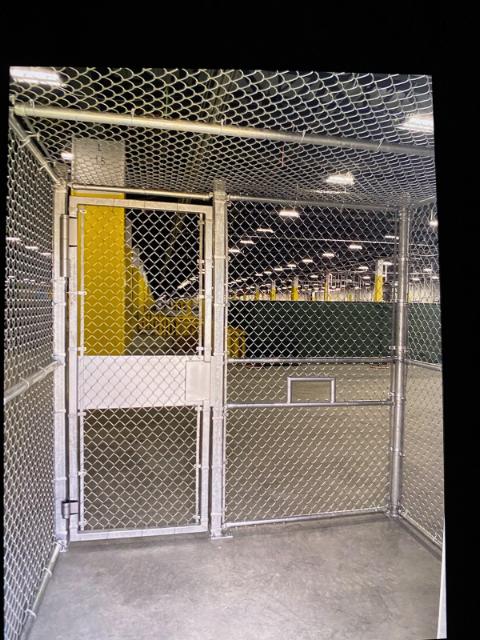 A chain-link security cage with a door, set in an industrial warehouse.