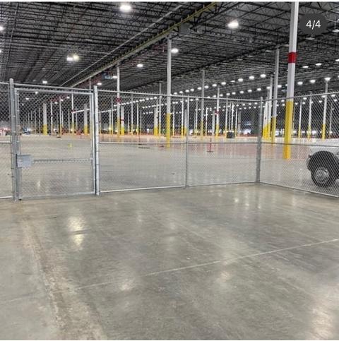 Chain-link fenced area inside a large, empty warehouse with concrete floor and support columns.