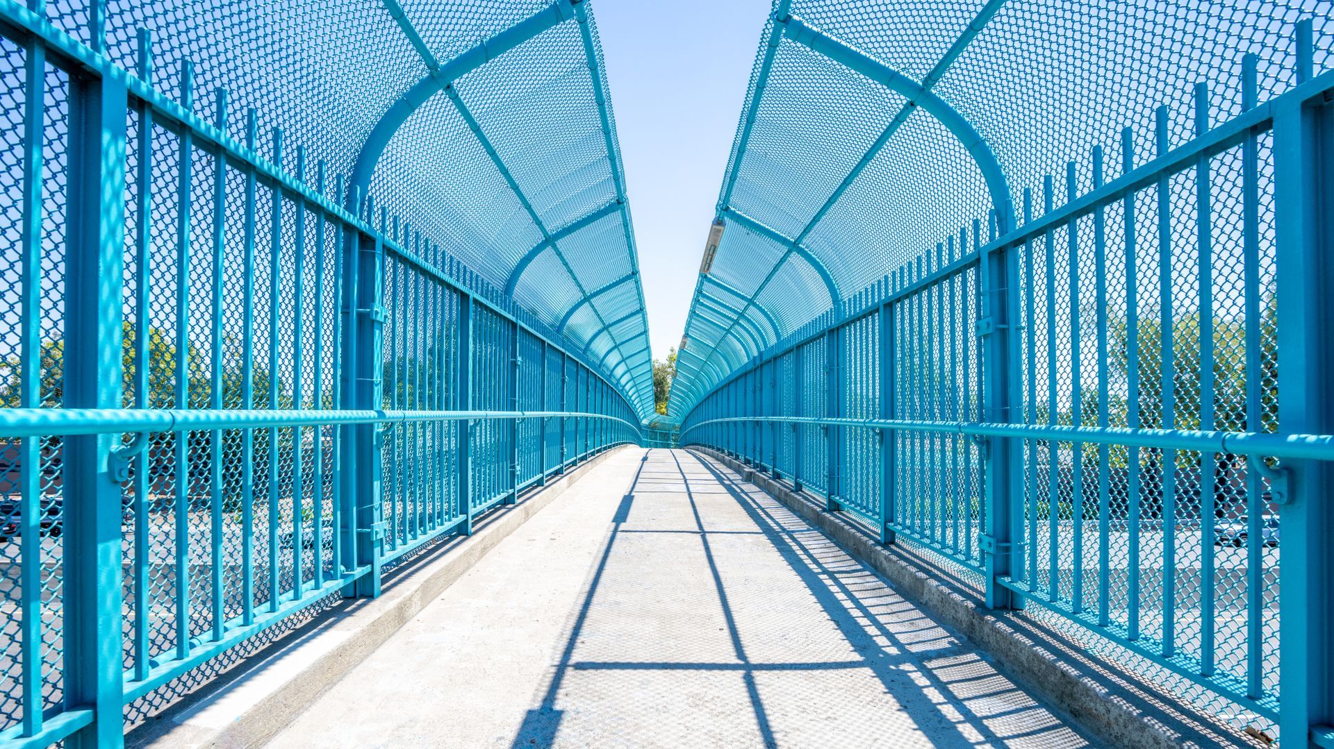 Blue pedestrian bridge, overhead netting, bright sky.