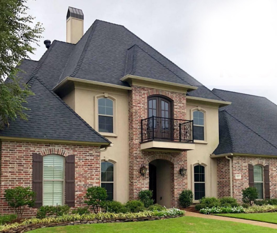 A large brick house with a black roof and a balcony