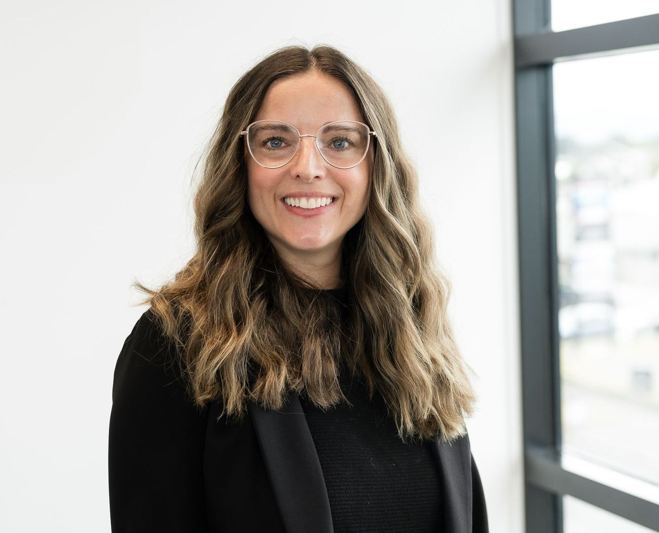 Nicola French wearing glasses and a black shirt is smiling in front of a window .