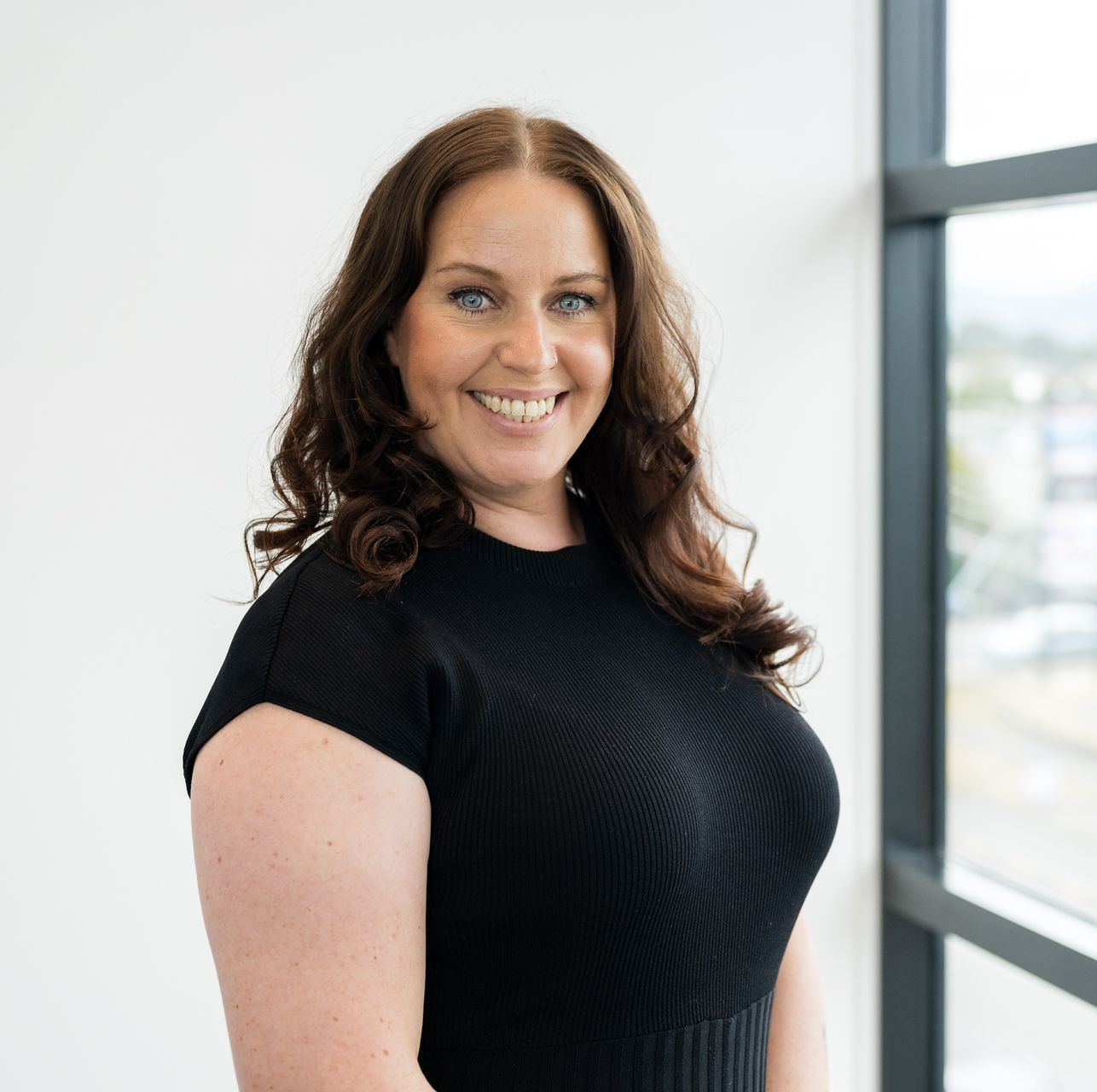 Erin Neale with long hair is smiling while sitting in a red chair .