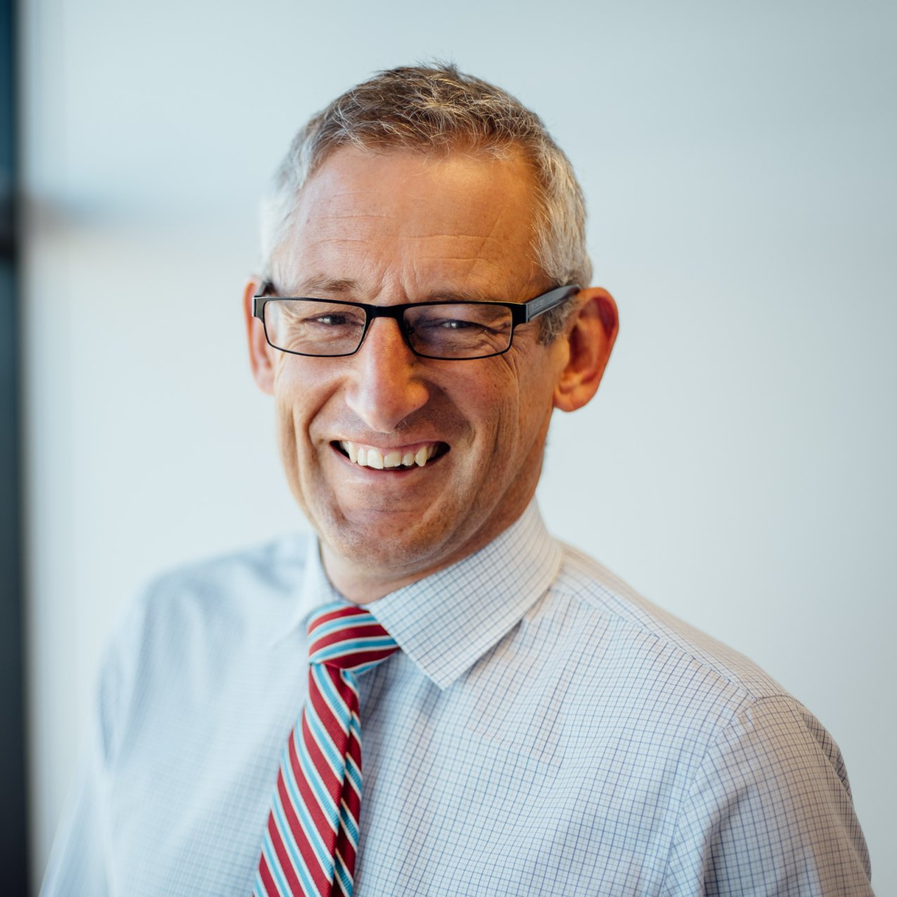 David Seath wearing glasses and a tie is smiling for the camera .