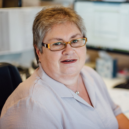 Jill Prentice wearing glasses is sitting at a desk in front of a computer .