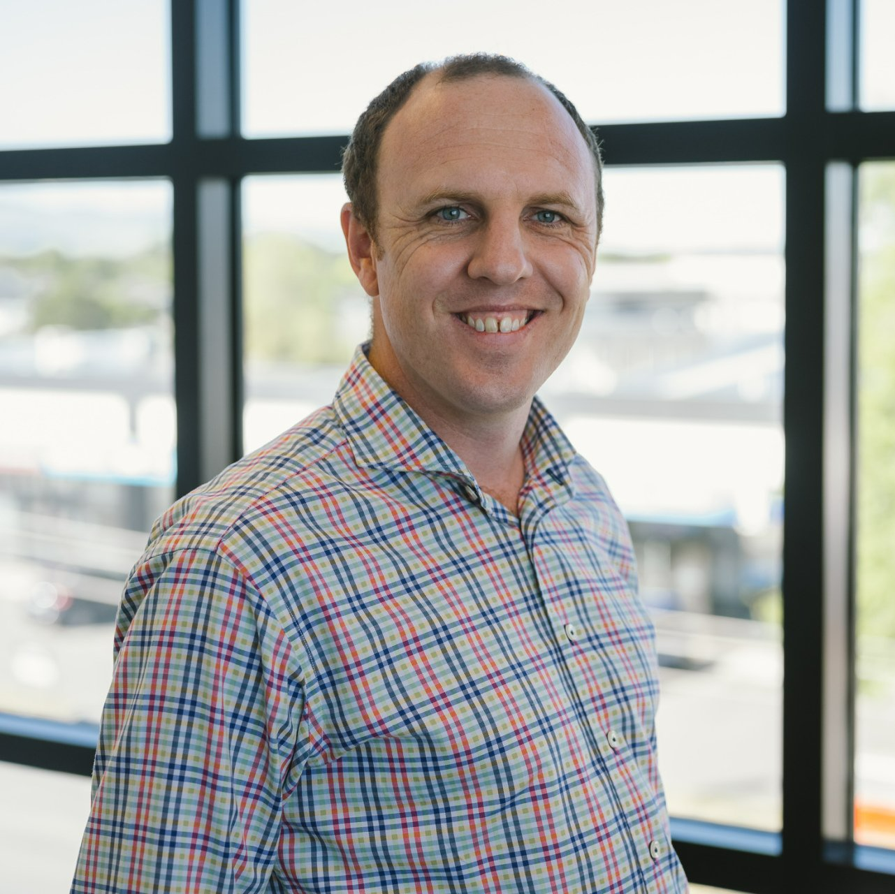 Tim Wade in a plaid shirt is standing in front of a window .