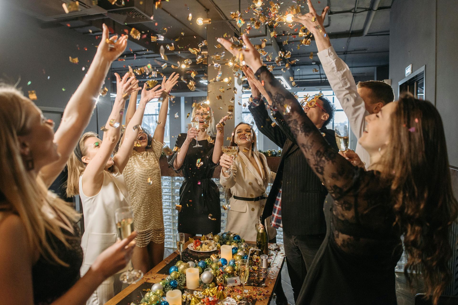People cheering with raised hands and sparklers around a decorated table indoors