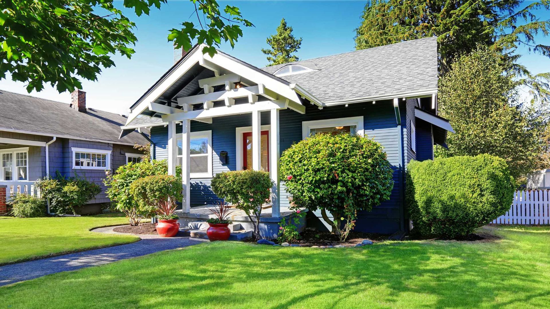 Blue bungalow with white trim and porch in a sunny, well-kept suburban yard