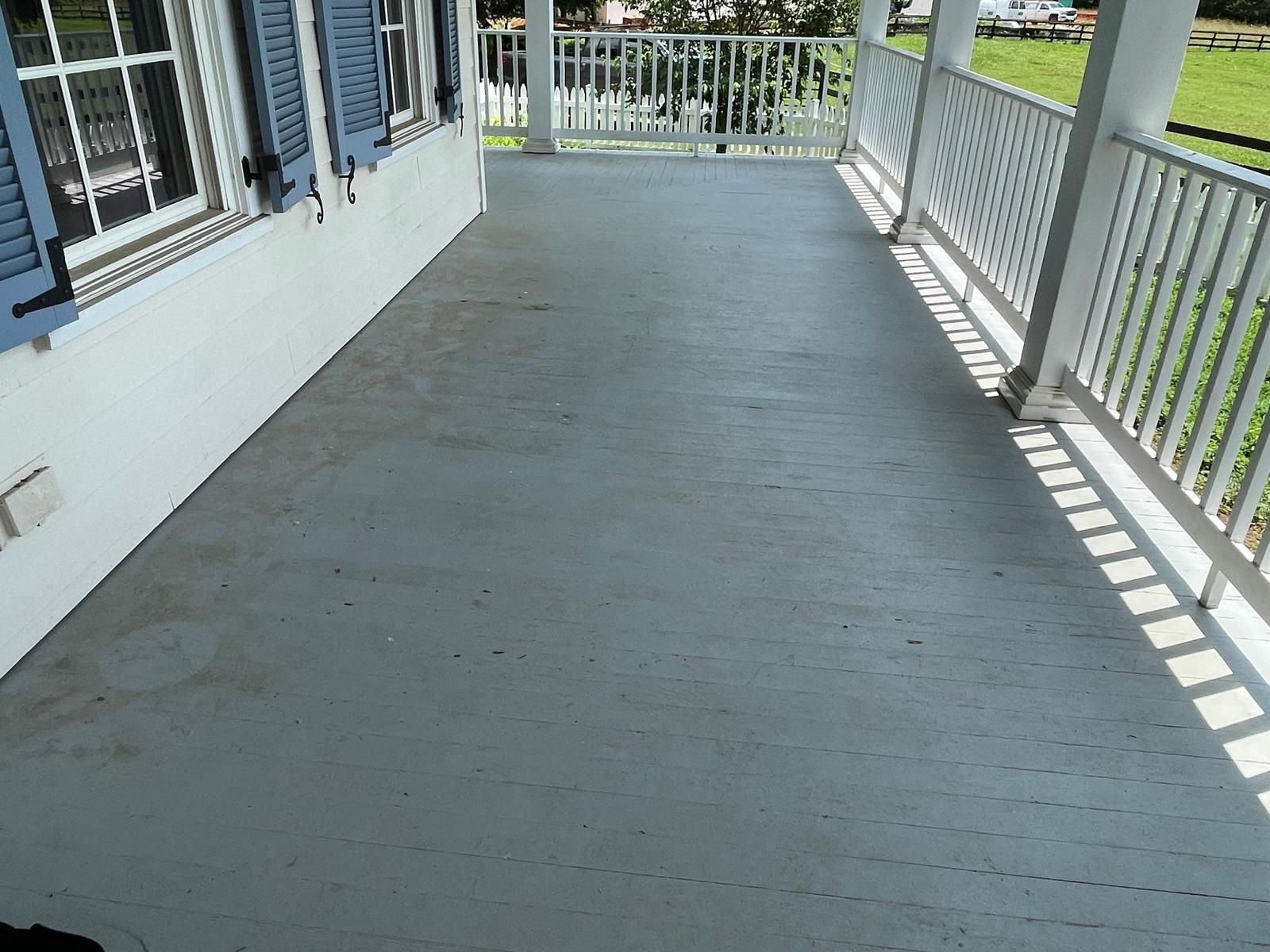 Empty gray porch with white railings beside a house, leading to a gate.