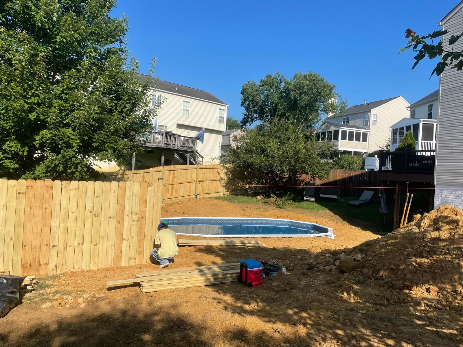 Backyard with above-ground pool, wooden fence, and neighboring houses on a sunny day