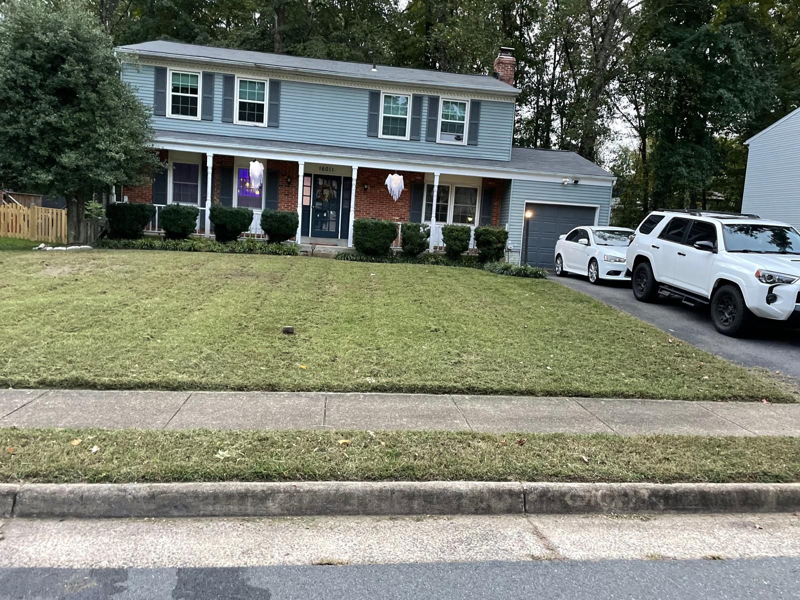 Suburban two-story blue house with white SUV in driveway and neatly trimmed front lawn