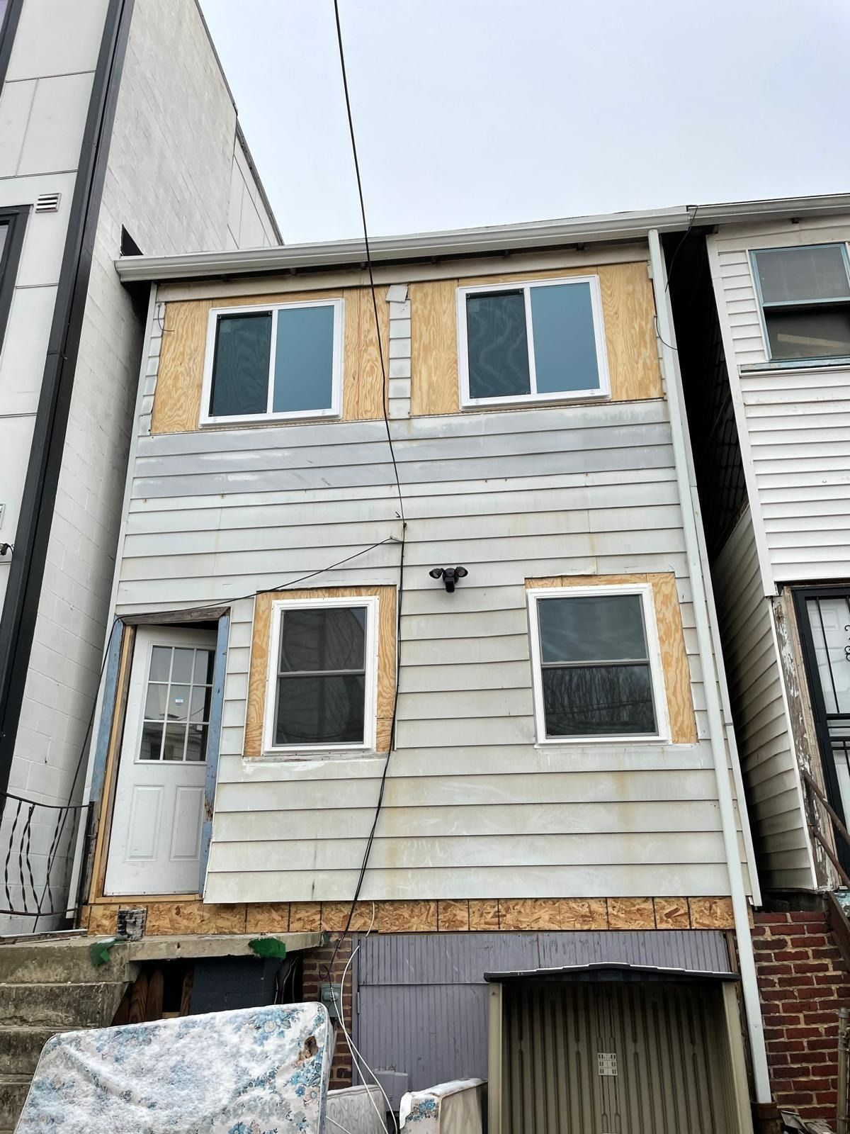 Narrow two-story house with white siding and tan trim, seen between neighboring buildings.