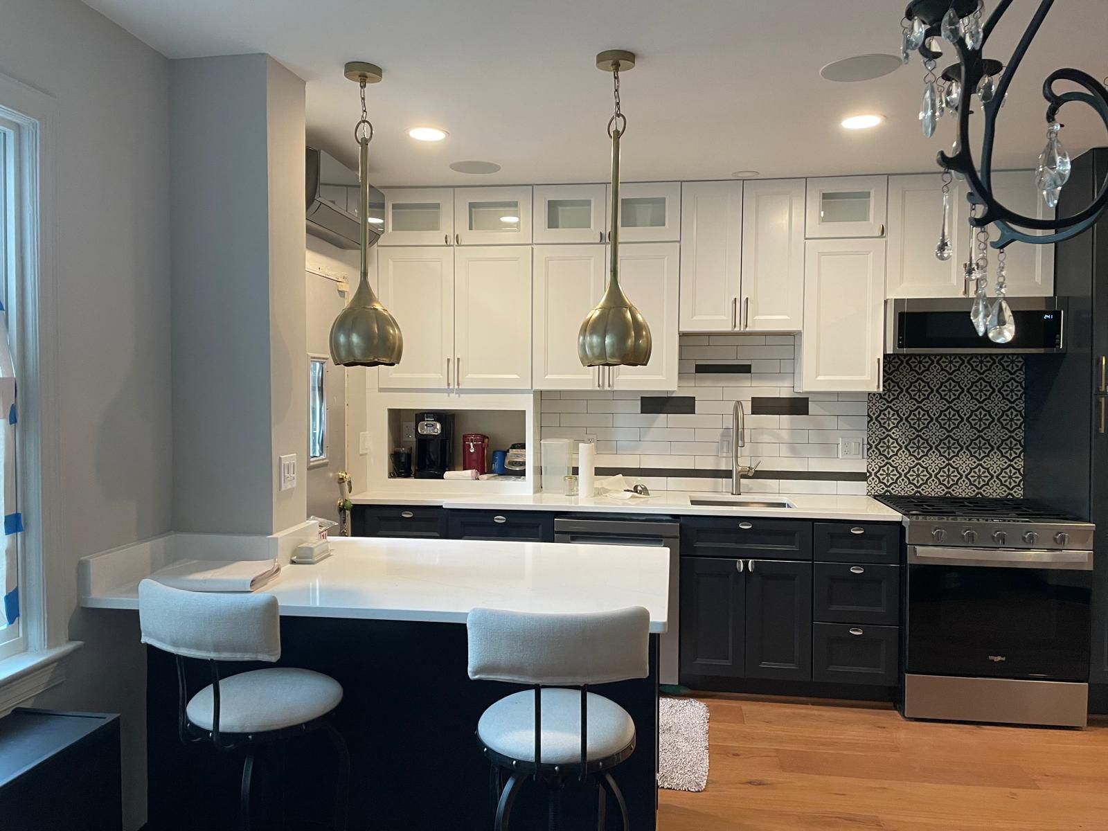 Modern kitchen with white cabinets, dark island with two stools, pendant lights, and stainless steel appliances