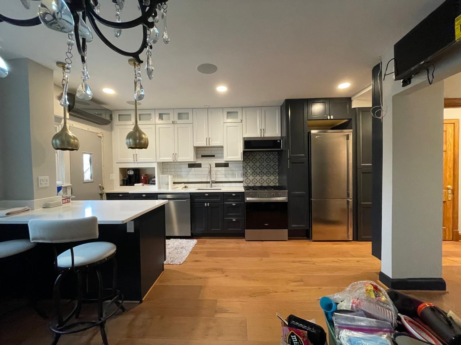 Modern kitchen and dining area with white cabinets, black appliances, wood floors, and hanging pendant lights