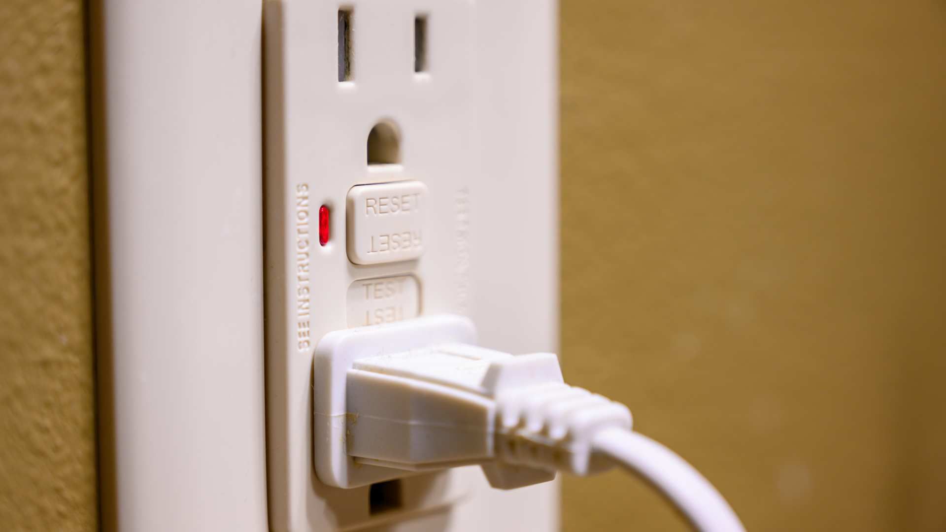 White power strip with a plugged-in cord against a beige wall