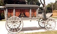 A decorated horse-drawn carriage with large wheels, shown outdoors on a sunny day.