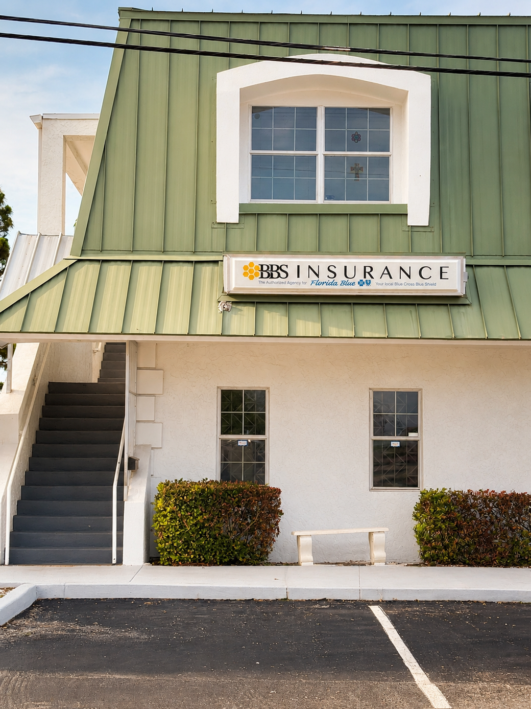 Two-story insurance office with green roof, exterior stairs, and parking spaces in front