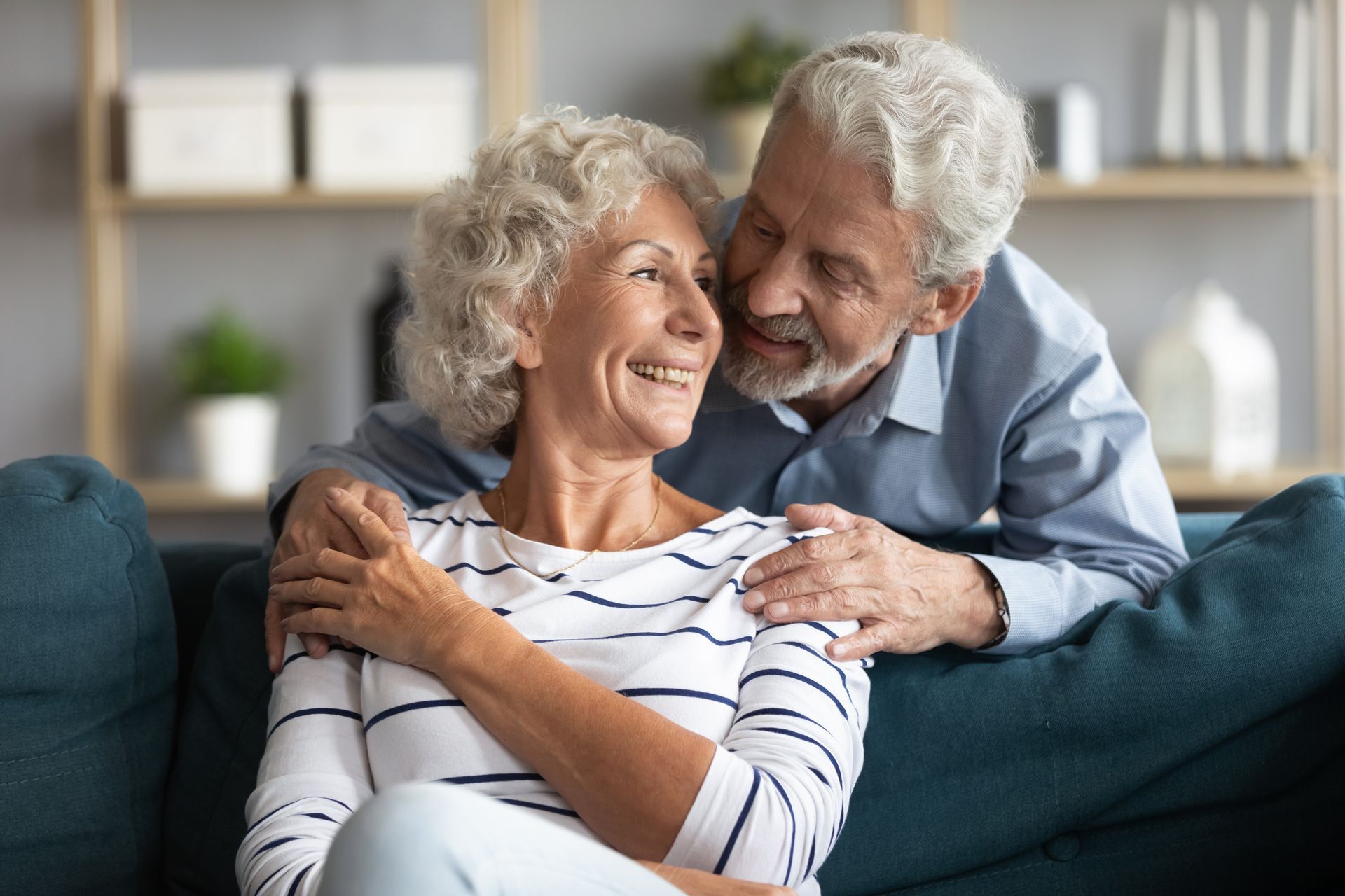 Smiling couple sitting on a blue couch, embracing in a cozy living room