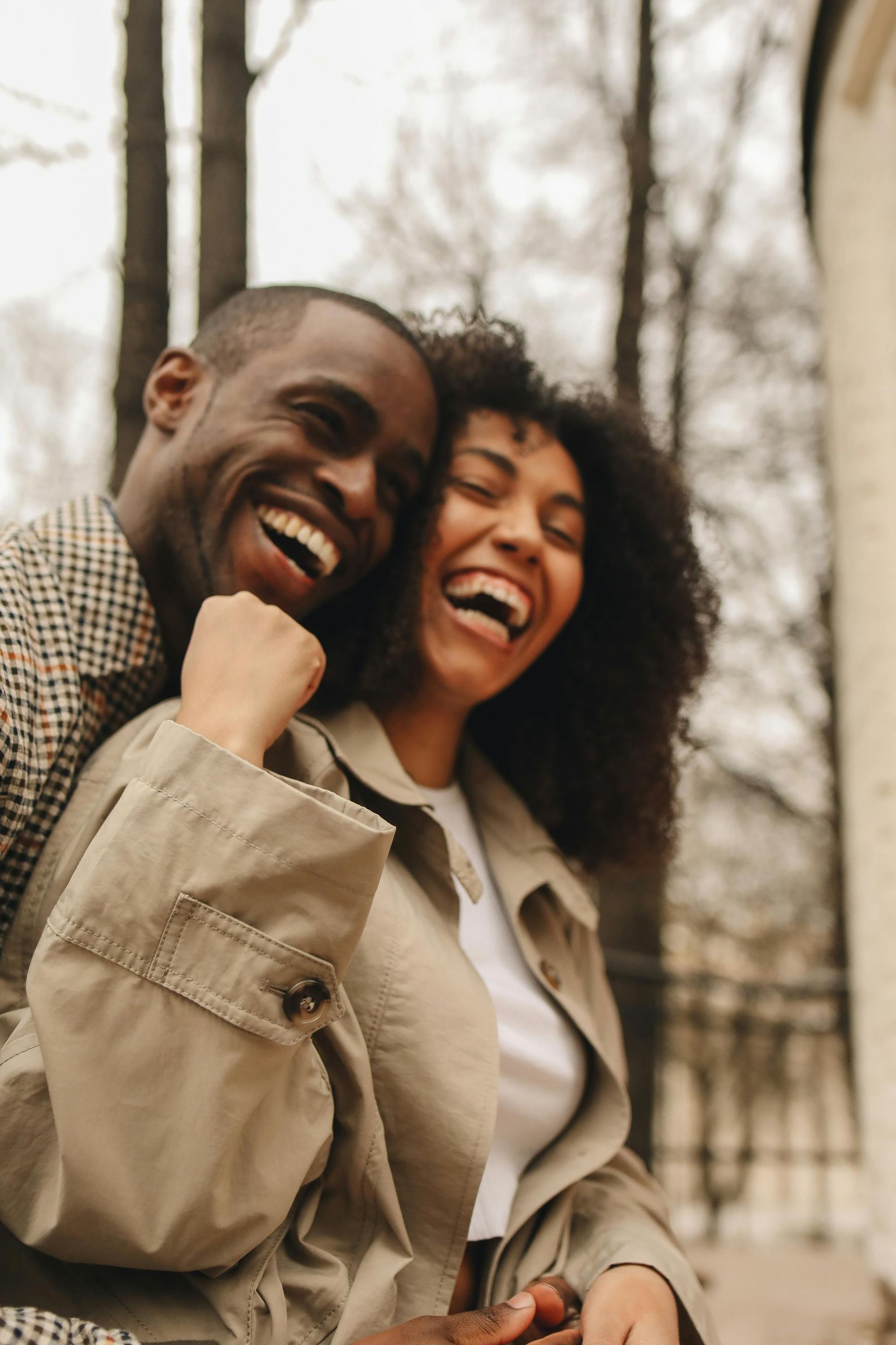 Two smiling people in beige jackets standing close together outdoors.
