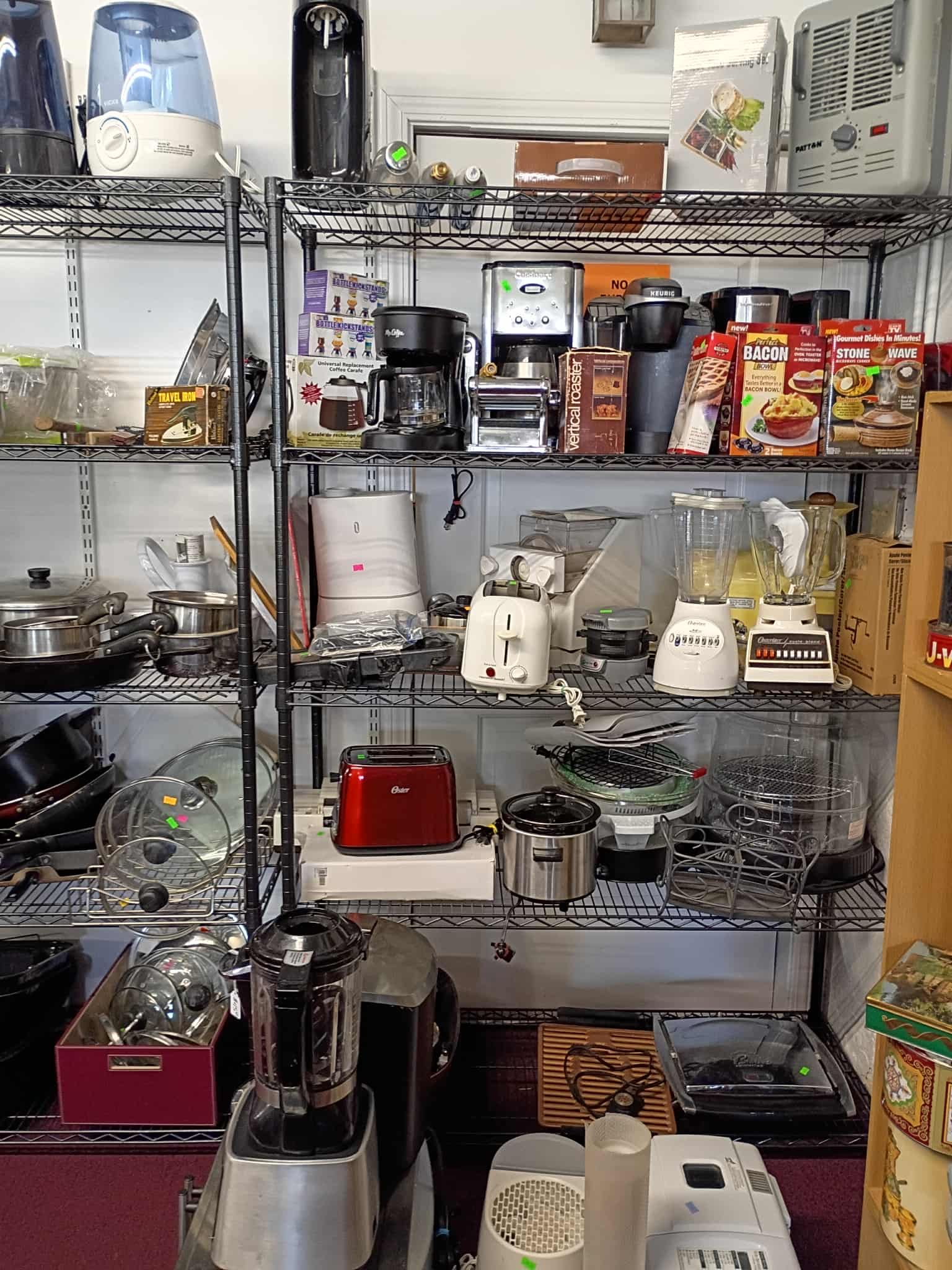 Shelves in a thrift store display kitchen appliances, including coffee makers, toasters, and blenders.