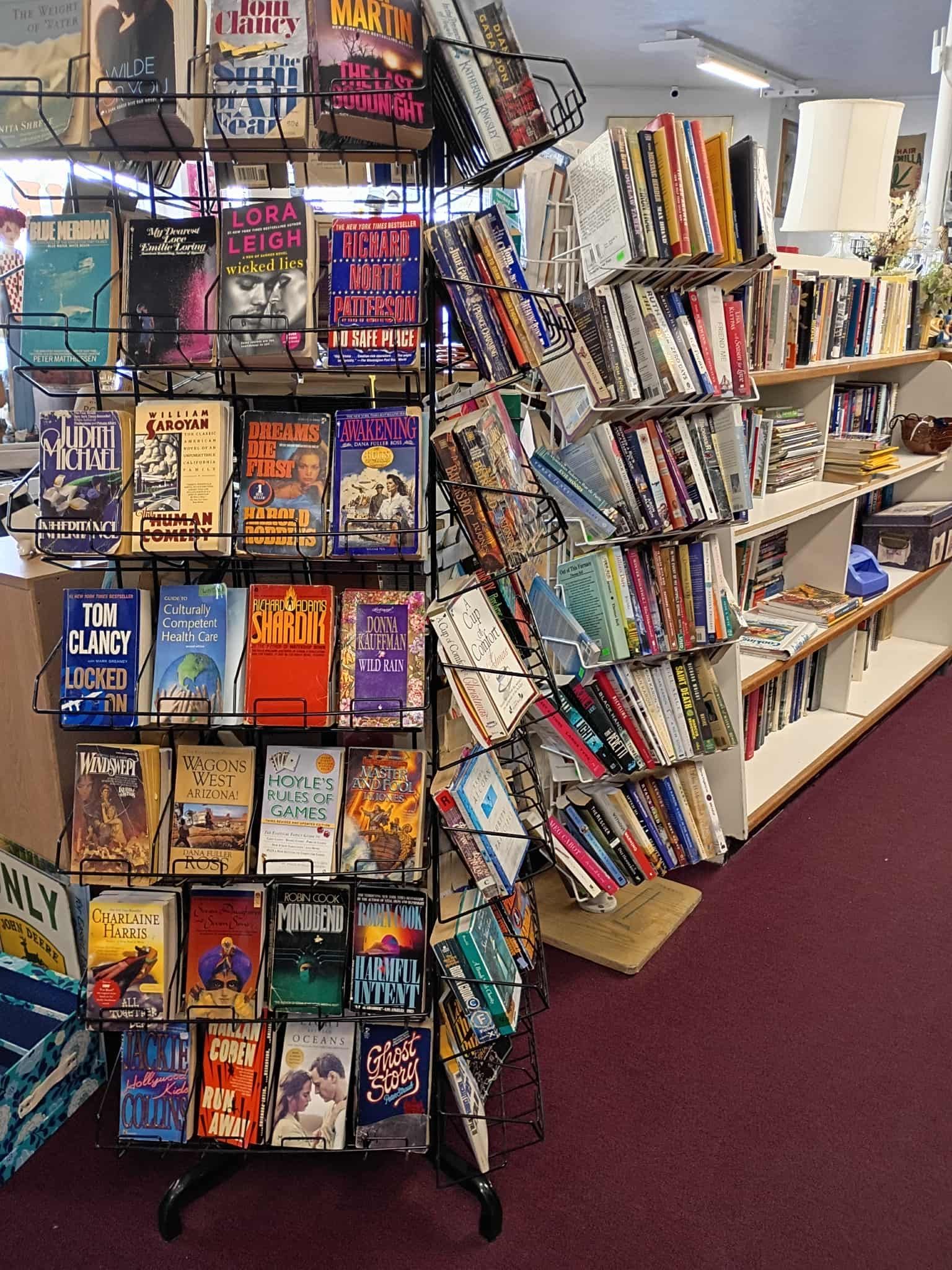 Bookshelves in a store. Wire rack with colorful books, white shelves in background. Purple carpet.