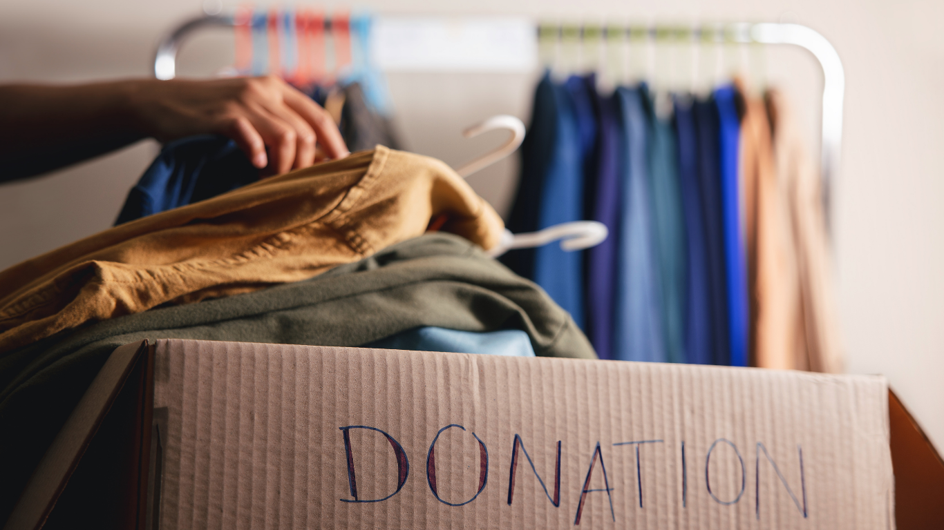 Cardboard donation box with clothing being placed inside.