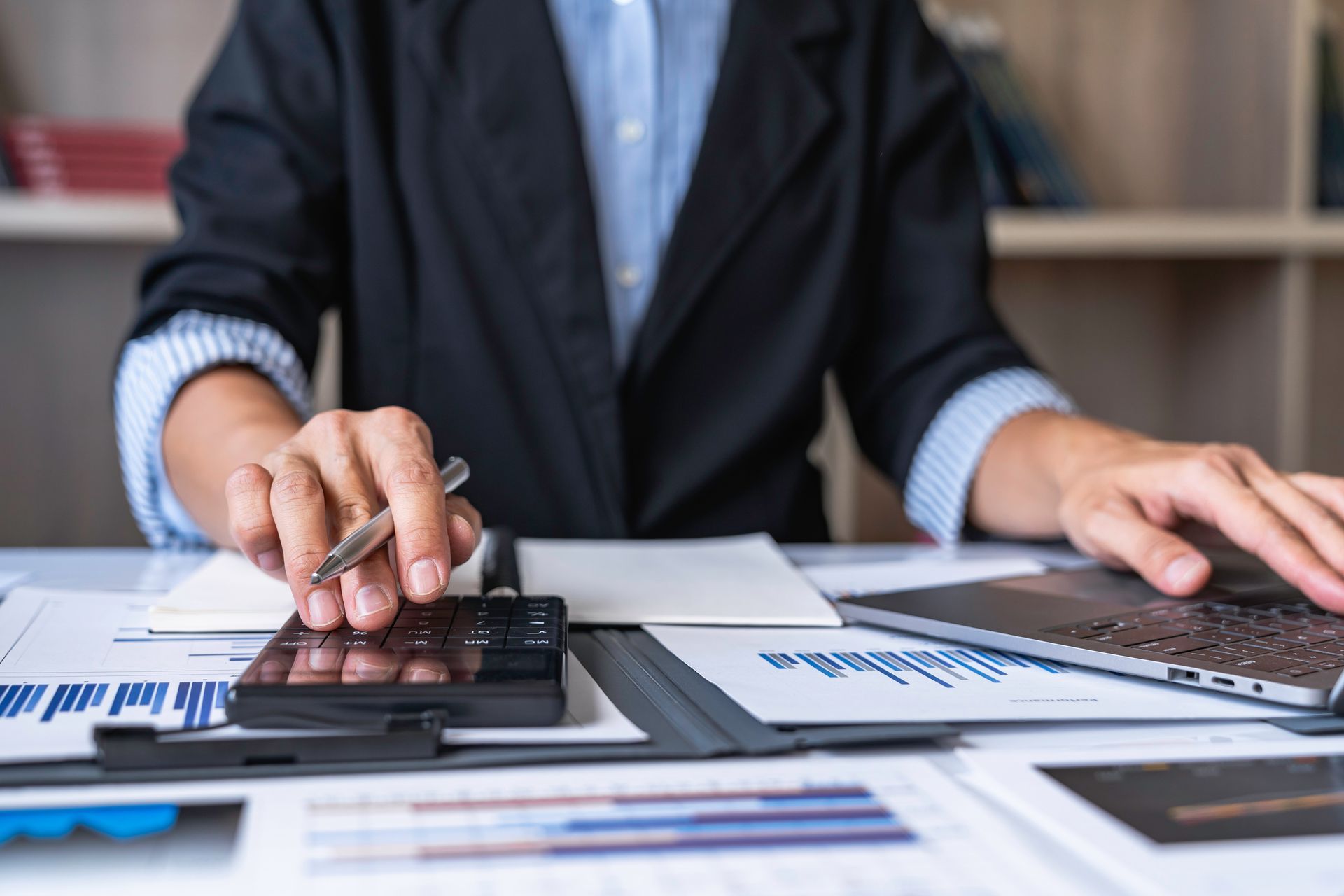 Close-up of hands using a calculator and reviewing documents next to a laptop. Close-up of hands using a calculator and reviewing documents next to a laptop.