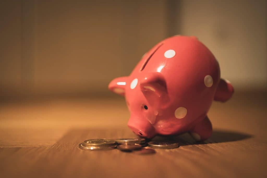 Pink polka-dotted piggy bank tipped over, coins spilling onto wooden floor.