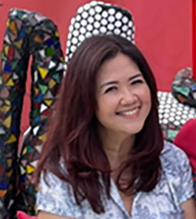 Woman smiling at the camera, brown hair, light blue top, red background with art.
