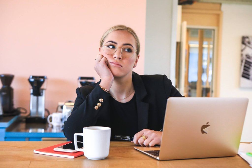 Woman at desk, looking bored, with laptop and coffee mug.