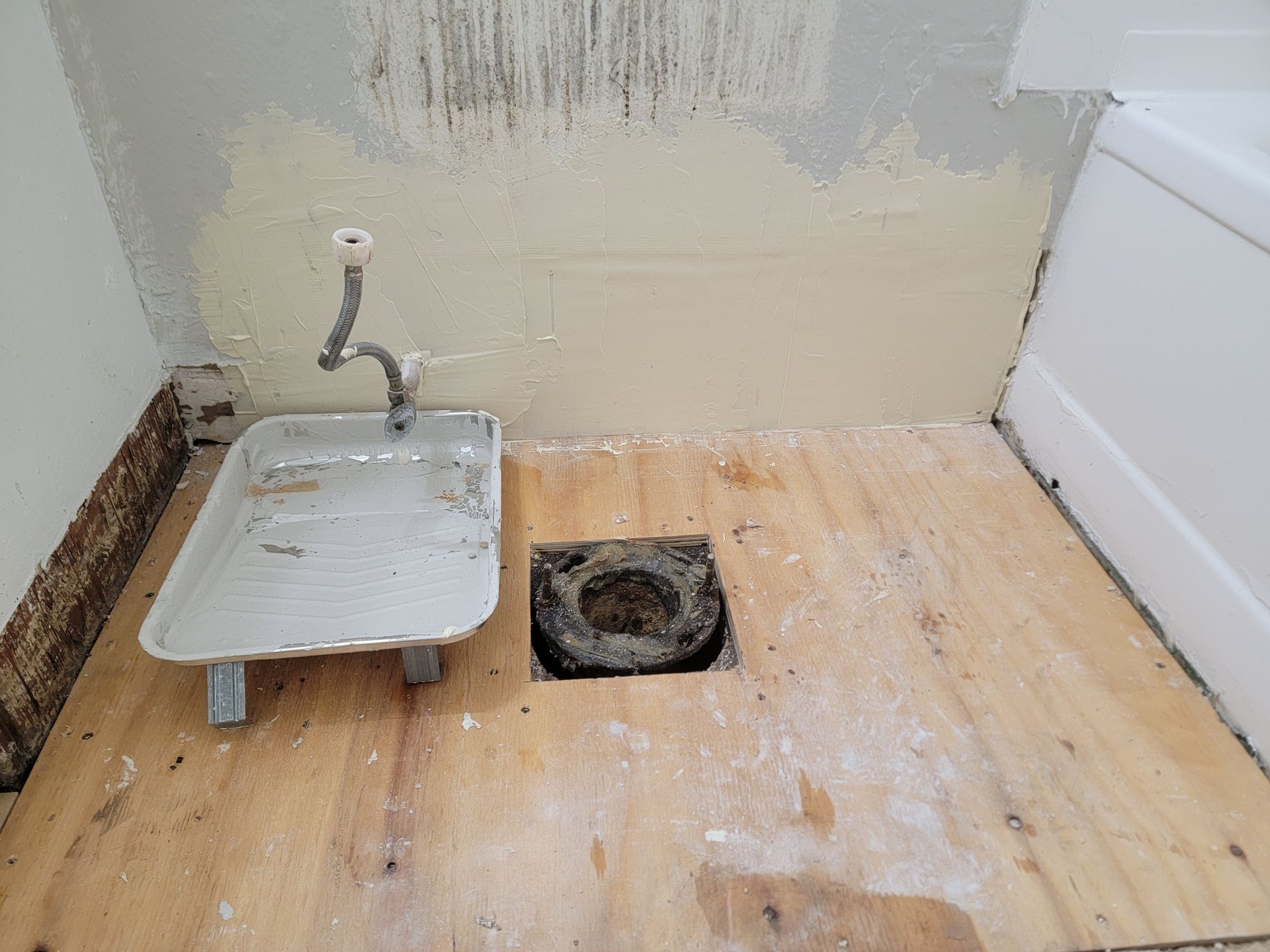 Small utility room with a sink, exposed drain hole, and unfinished wooden floor.