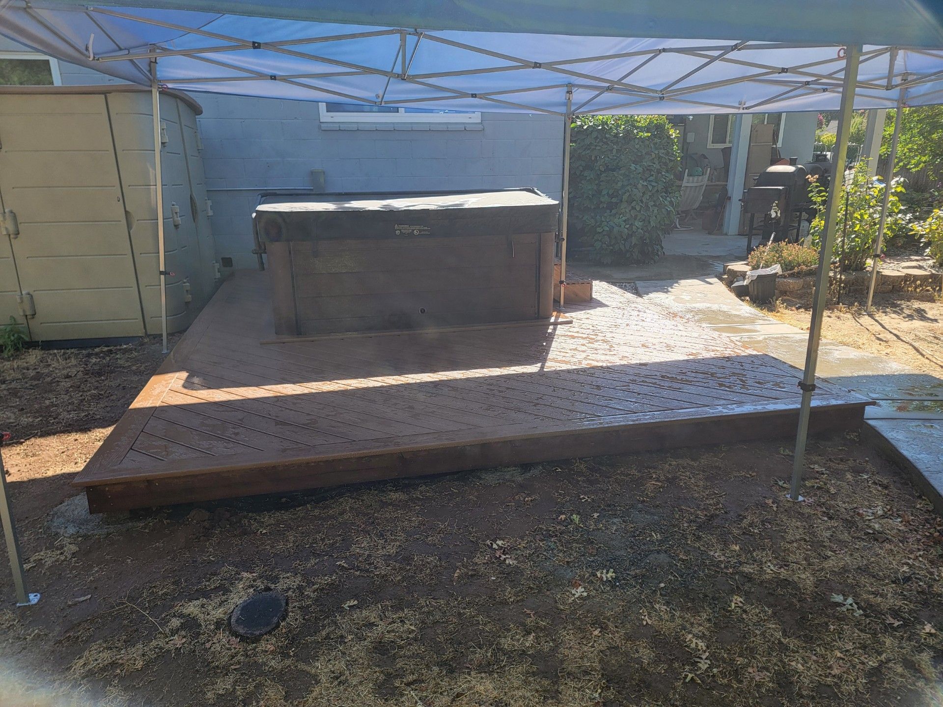Backyard patio with a raised wooden deck, canopy frame, and storage shed in bright sunlight