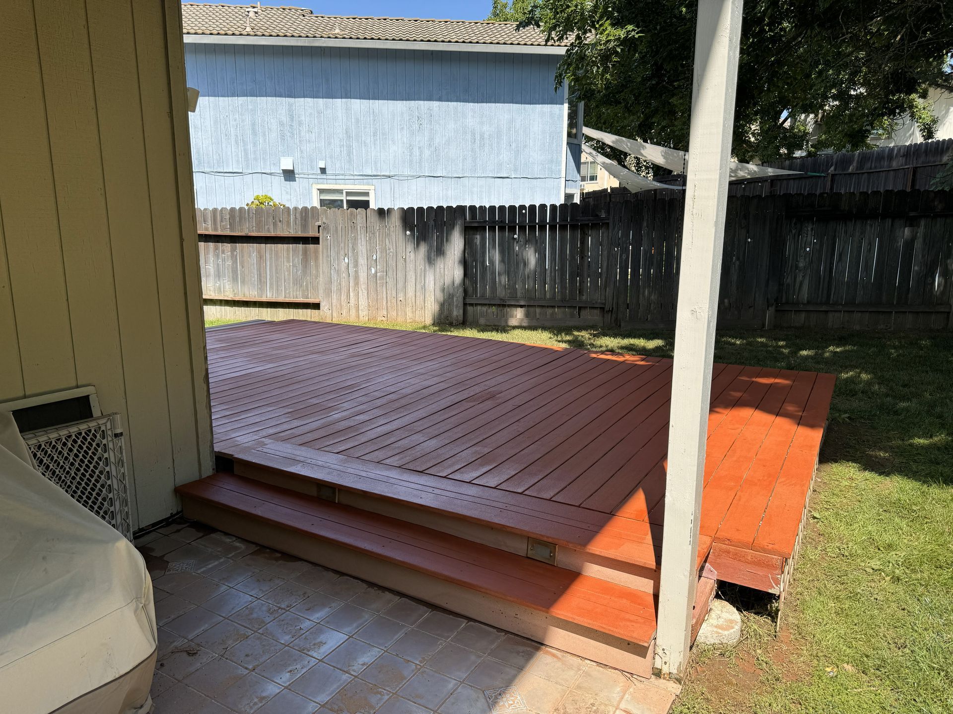 Backyard wooden deck ramp with orange steps, beside a fenced yard and carport support post