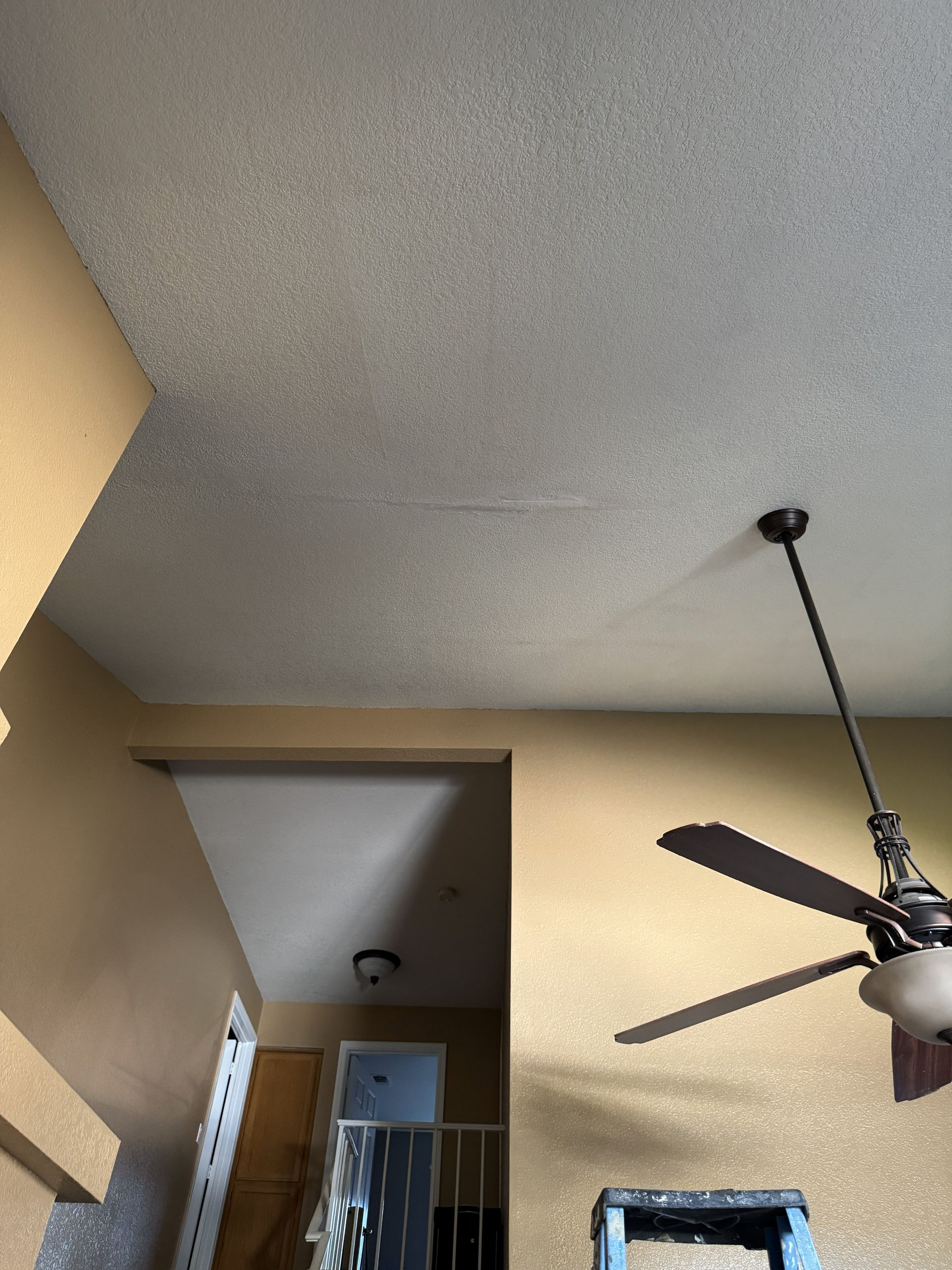 Ceiling and hallway corner with a black ceiling fan and beige walls near a stairwell