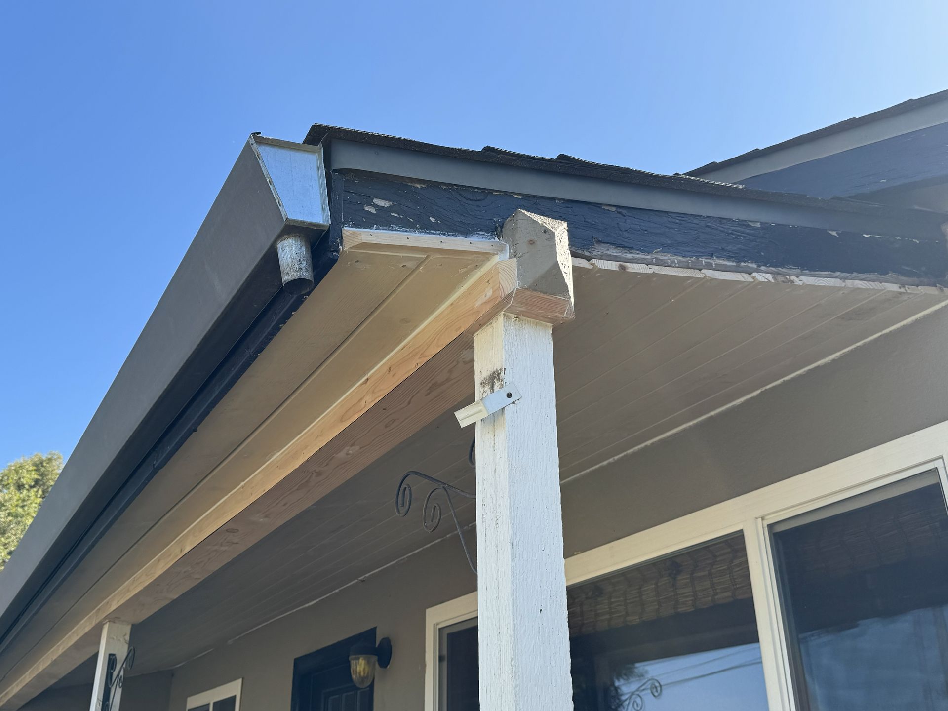 Close-up of a house roof eave and porch support against a blue sky.