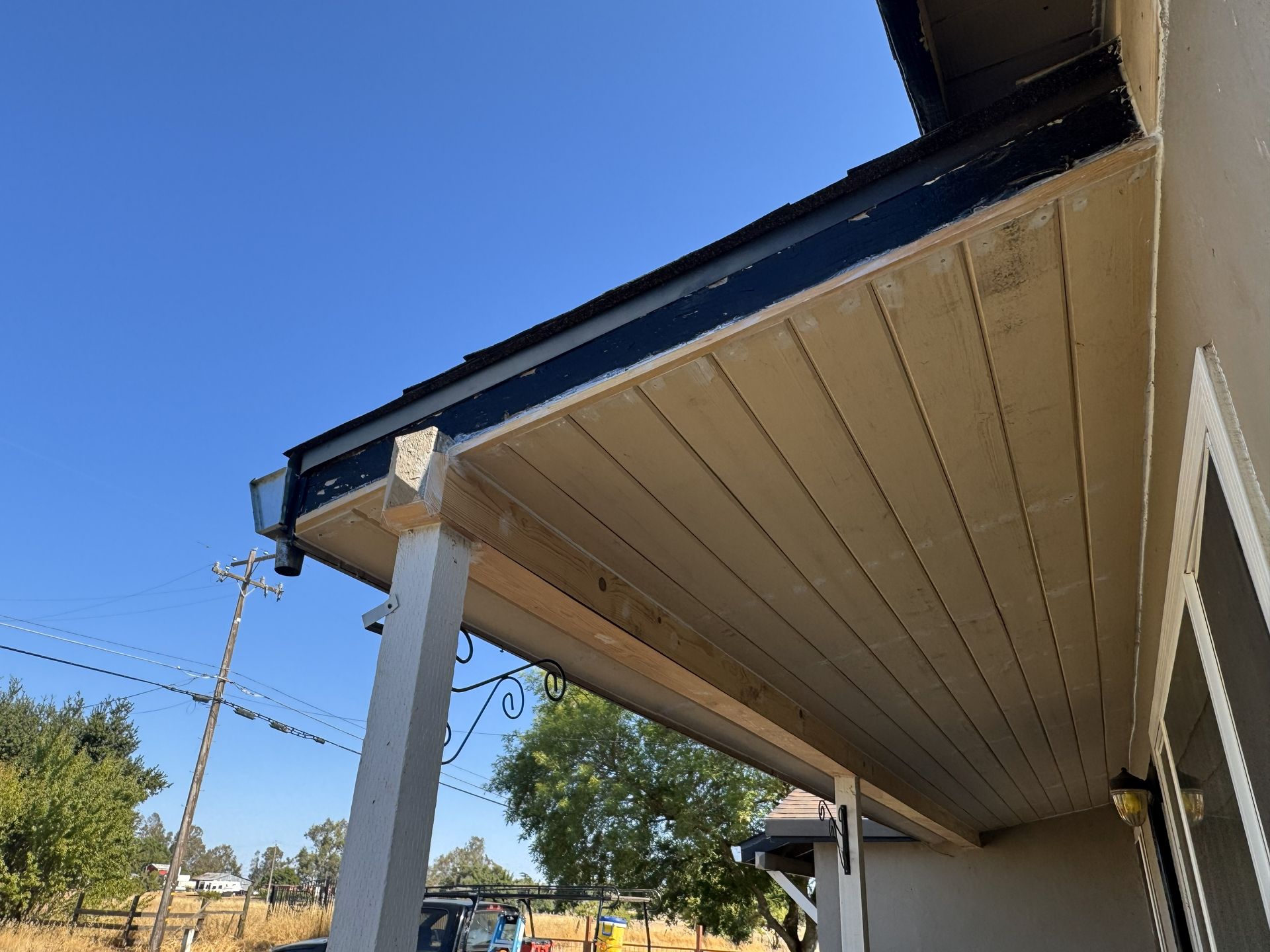 Low-angle view of a house roof eave and porch post against a clear blue sky