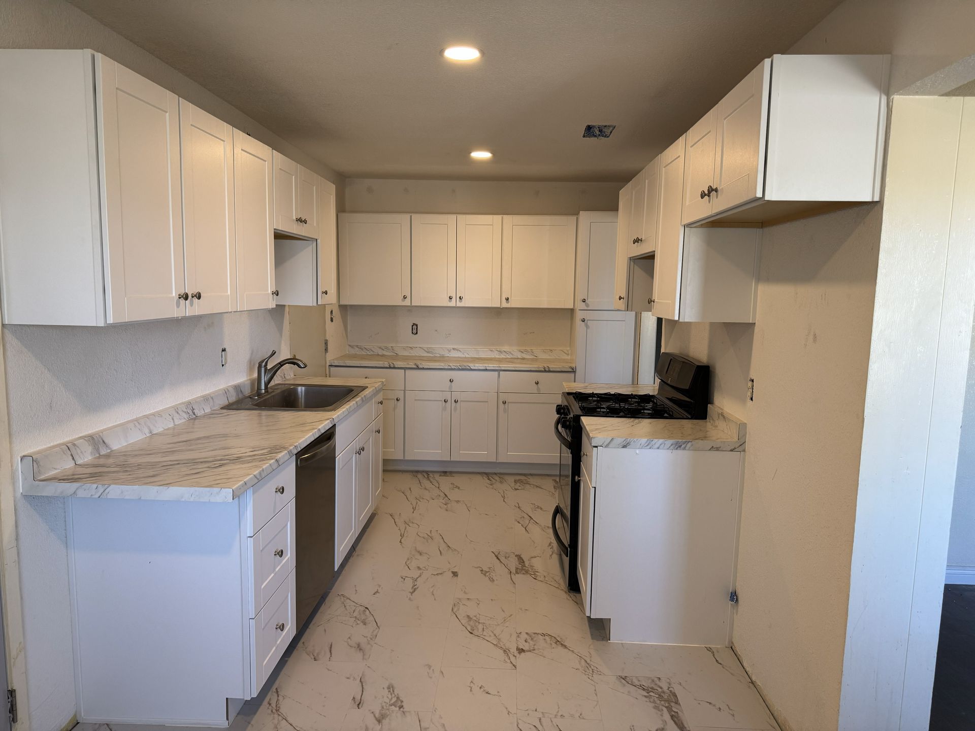 Bright white galley kitchen with marble countertops, white cabinets, and a stove by the right wall.