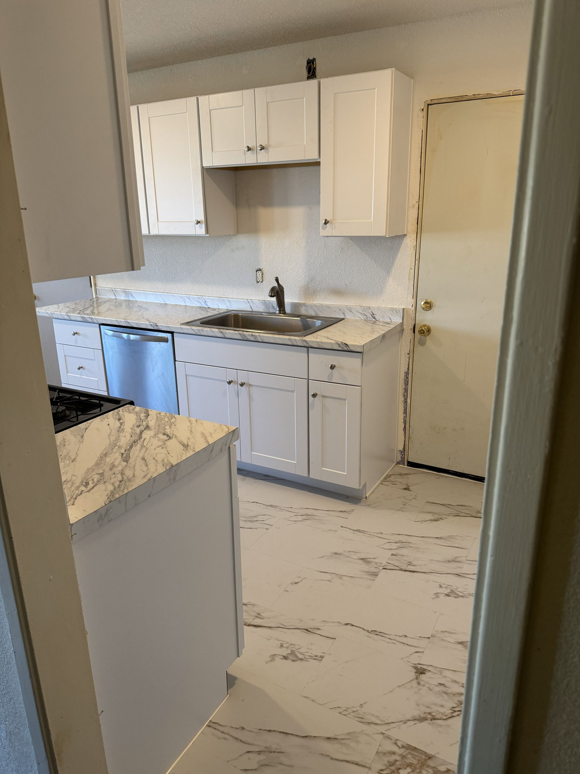Empty kitchen with white cabinets, marble-pattern counters, and a stainless sink and dishwasher.