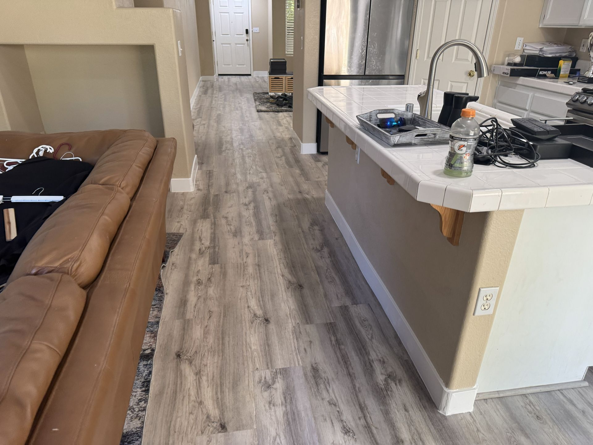 Kitchen and living area with brown sofa, island counter, and wood-look flooring leading to a hallway