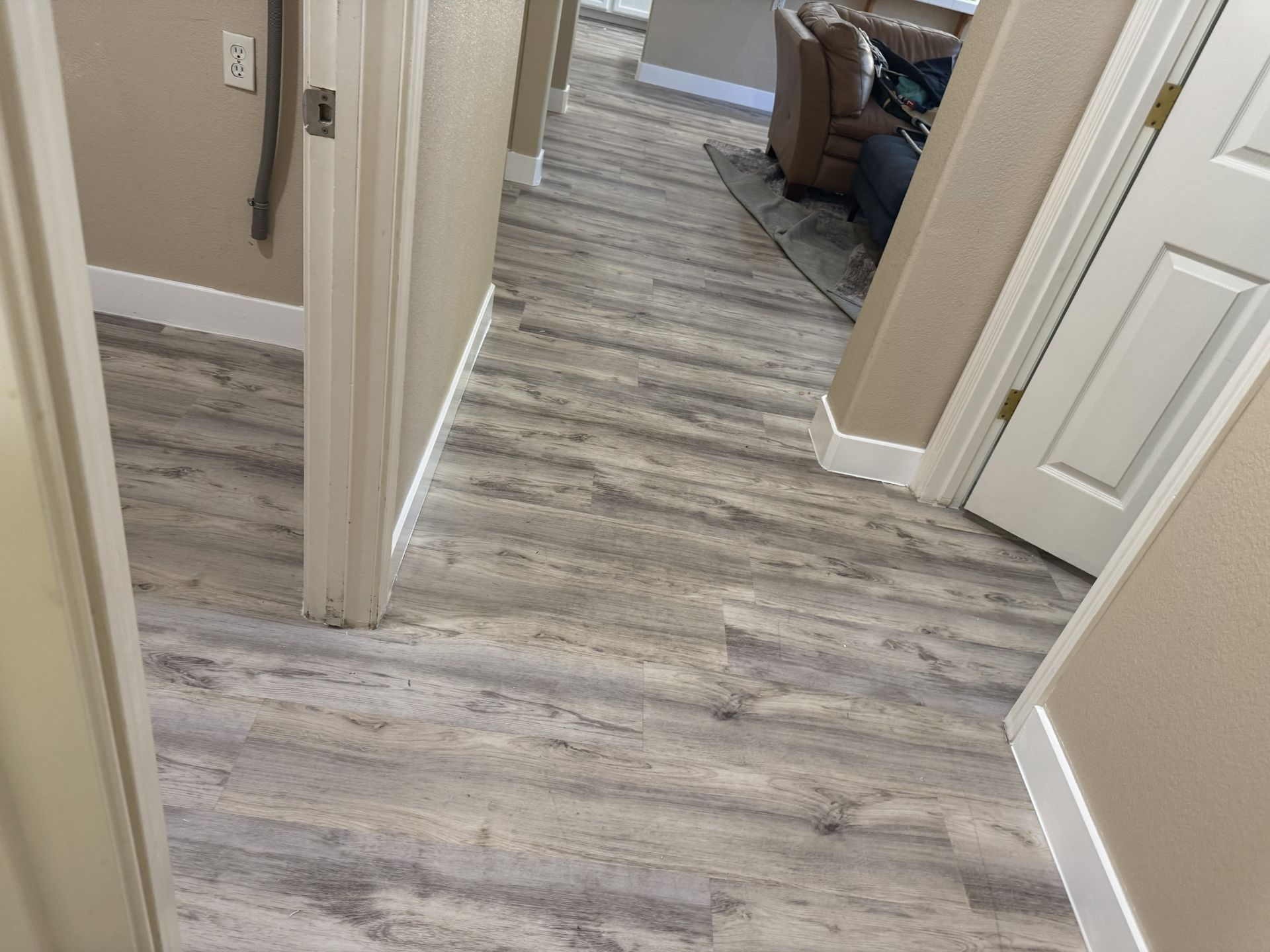 Hallway with gray wood-look flooring, beige walls, and doorways leading to a living room.
