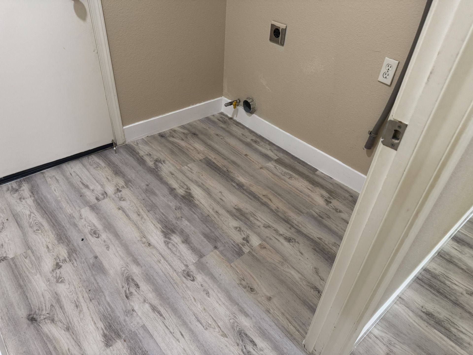 Empty beige room with gray wood flooring and a doorway on the right.
