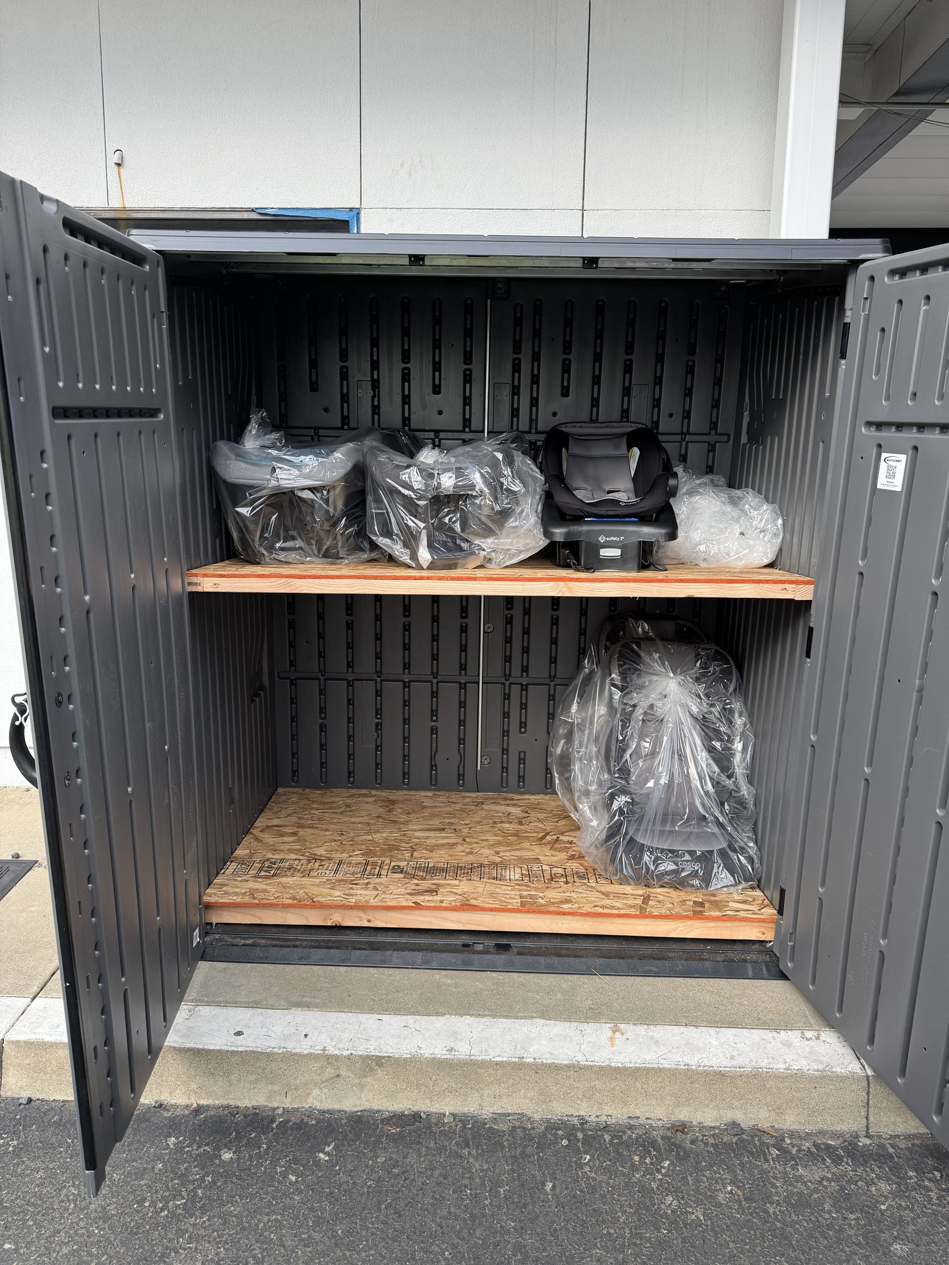 Shelved storage unit with wrapped items, wooden planks, and a black container in a gray metal shed