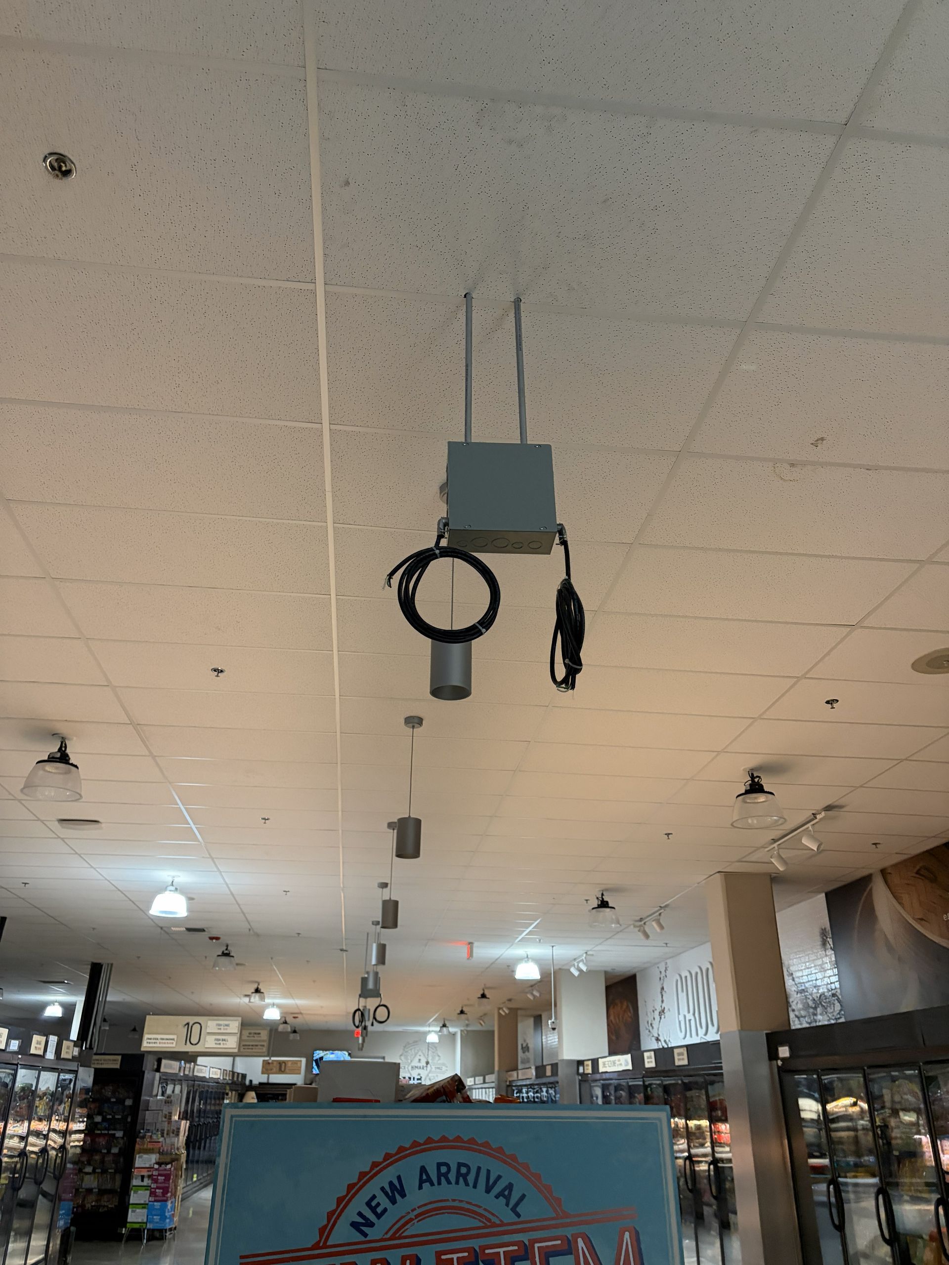 Retail store ceiling with a hanging security camera and cables, aisles visible below