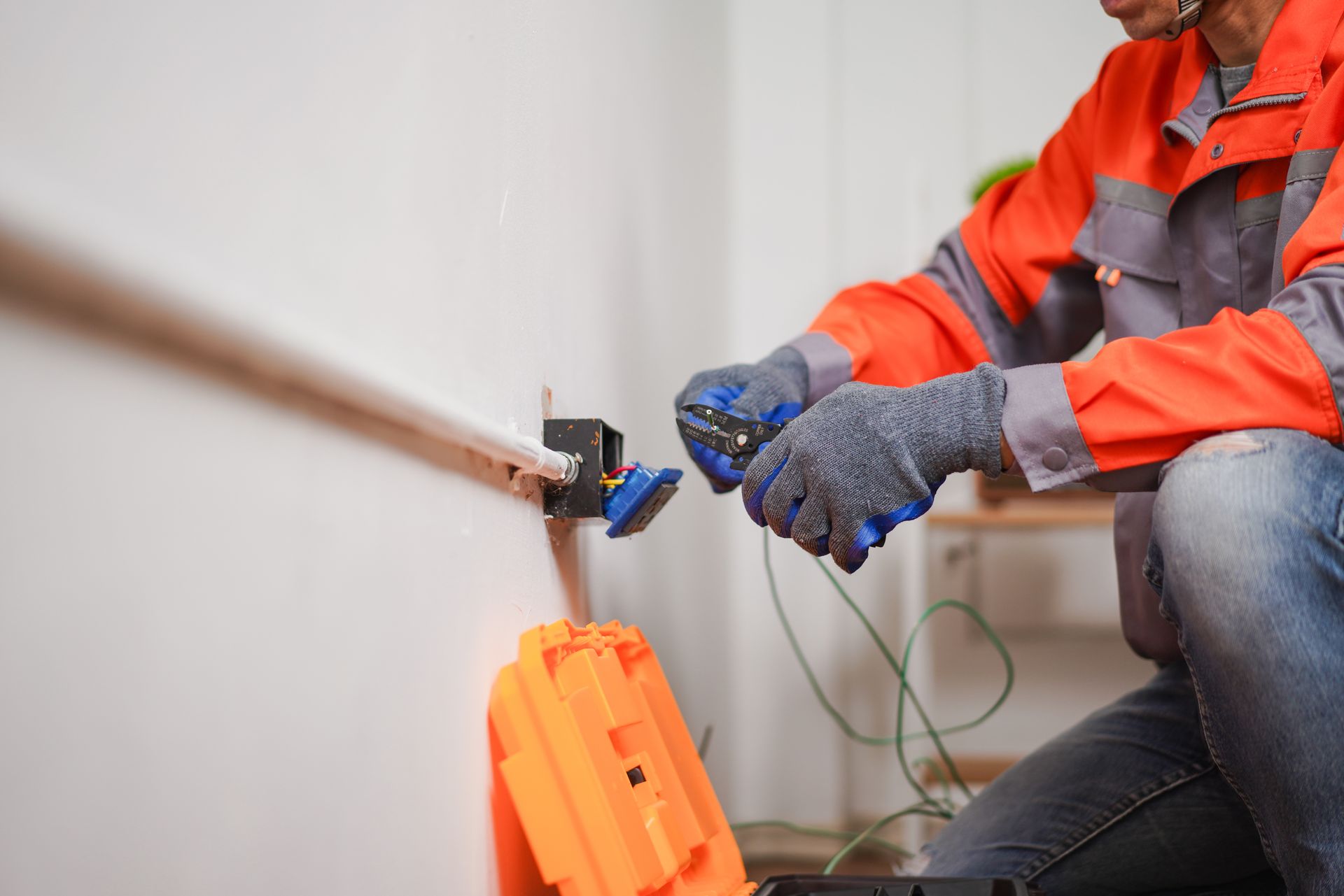 A residential electrician fixing an electrical outlet in a home with tools and safety gear.