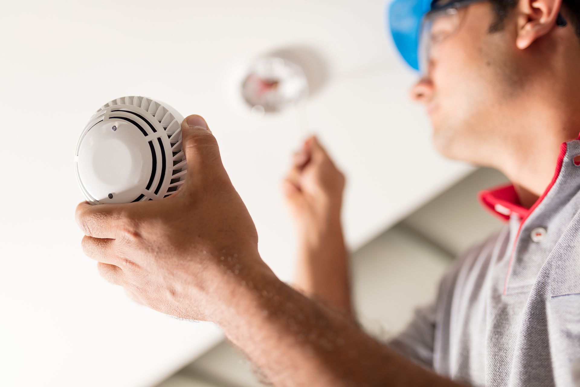 Person installing a white smoke detector on a ceiling with a screwdriver