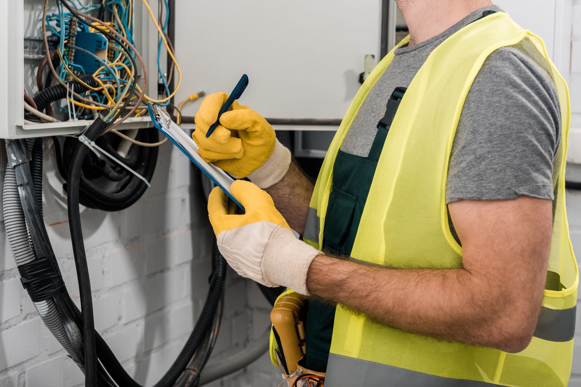 Technician in yellow vest testing wiring in an electrical panel with a multimeter